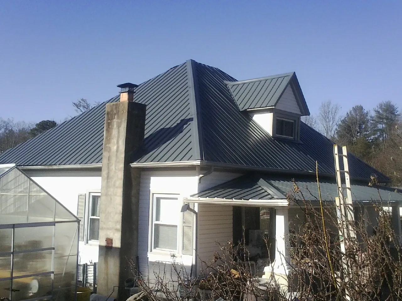Dark blue standing seam metal roof on a white farmhouse with dormer — Slate & Tile Roof Repair by Roofing Brothers in Mulino