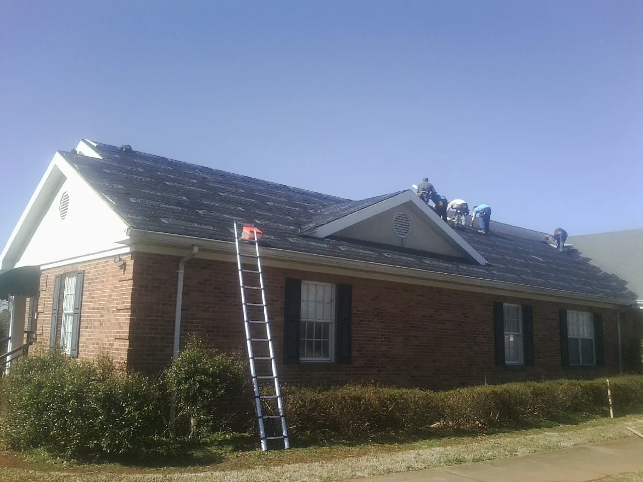 Crew tearing shingles off a brick ranch roof with a ladder set — Metal Roof Repair work by our crew in Mulino