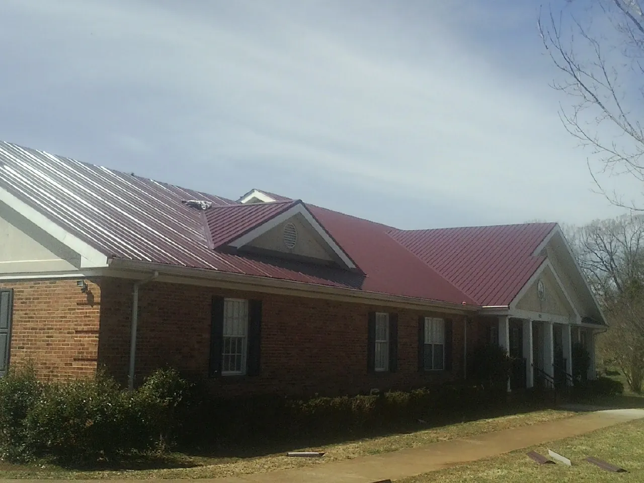 Red metal roof with gabled entries on a long brick building, from a Hail Damage Roof Repair job in Mulino