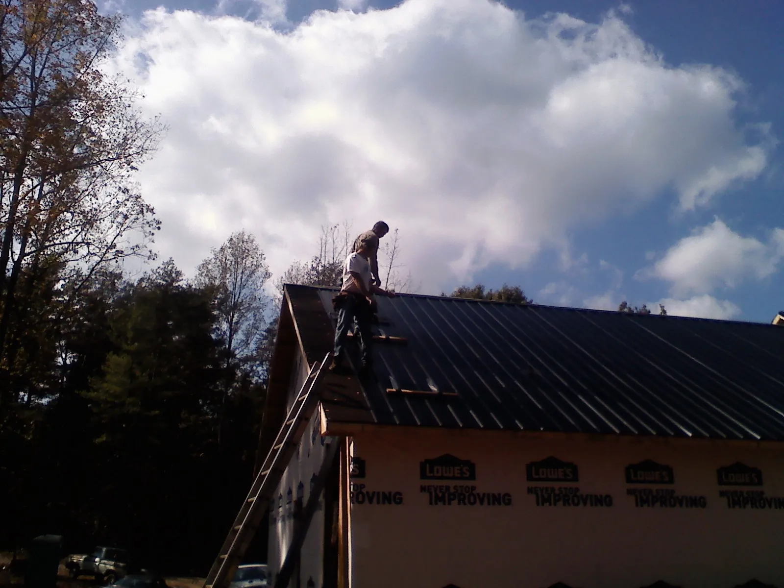 Roofer fastening dark metal panels high against a cloudy sky, from a Roof Inspection job in Mulino
