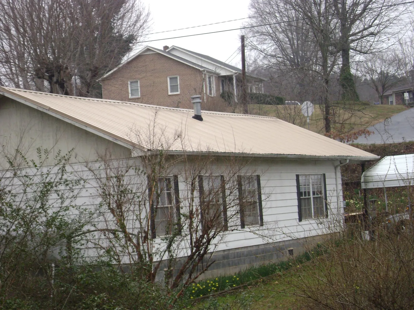 Tan metal roof on a white sided house set into a hillside — Commercial Roofing by Roofing Brothers in Mulino